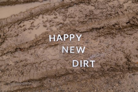 Foto de Las palabras feliz nueva suciedad con letras de metal plateado en la superficie de barro húmedo - Imagen libre de derechos