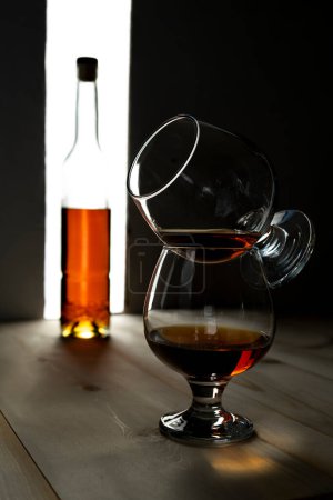 Photo for "Bottle and glass of cognac over dark and white background" - Royalty Free Image