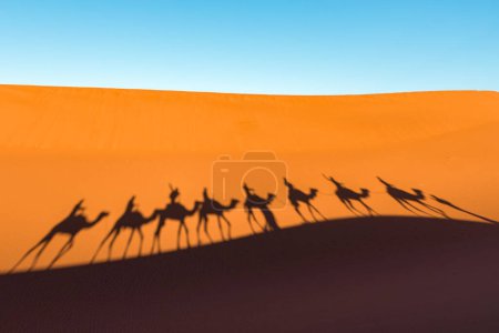 Foto de Brote diurno de gran angular de siluetas de caravana de camellos en dunas desérticas de Erg Chigaga, a las puertas del Sahara. Marruecos. Concepto de viaje y aventura. - Imagen libre de derechos