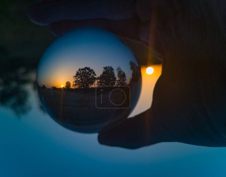 Foto de Sol naciente de la mañana atrapado en bola de lente cristalina con siluetas de árboles - Imagen libre de derechos