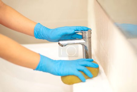 Photo for A hand in a blue rubber glove in the picture, removes and washes bathroom sink - Royalty Free Image