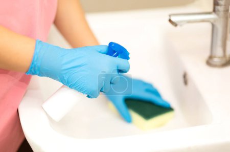 Téléchargez les photos : Personne, une main dans un gant de caoutchouc bleu dans l'image, enlève et lave lavabo de salle de bains - en image libre de droit