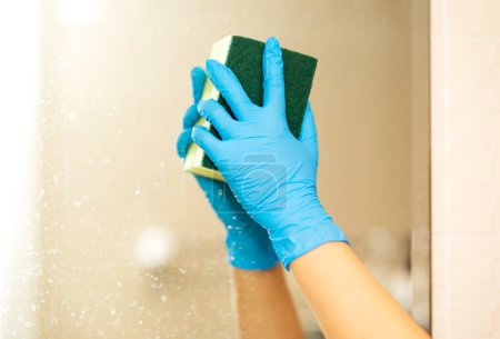 Téléchargez les photos : Une main dans un gant de caoutchouc bleu dans l'image, enlève et lave lavabo de salle de bains - en image libre de droit