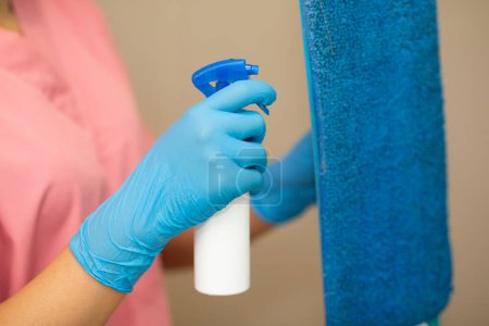 Photo for Close-up women hand in a blue rubber glove and cleaning spong in the picture, removes and washes bathroom sink and mirror. - Royalty Free Image