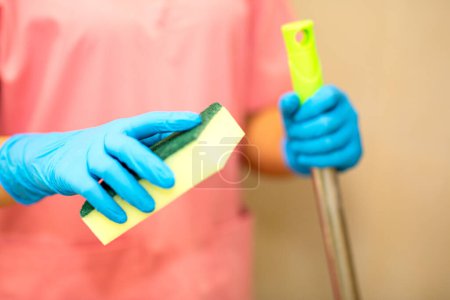Photo for Close-up women hand in a blue rubber glove and cleaning spong in the picture, removes and washes bathroom sink and mirror. - Royalty Free Image