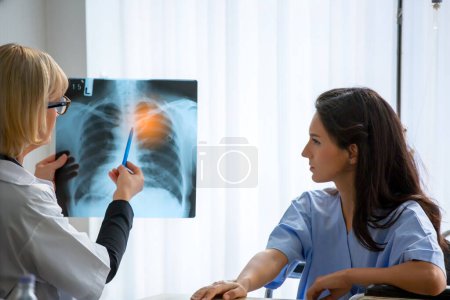 Photo for Doctor explaining lungs x-ray to women patient in clinic or Doctor in the office examining an x-ray and discussing with a patient - Royalty Free Image