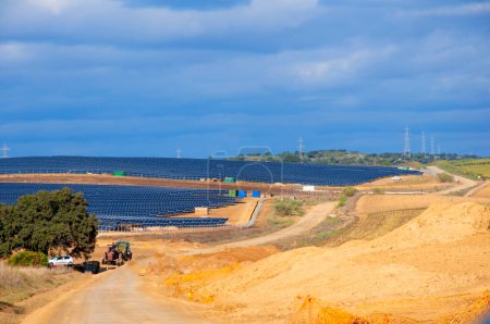 Photo for Big yellow land with solar panels on the left side , old fieldengine. Yellow dirt road and blue sky. Seville, Spain - Royalty Free Image