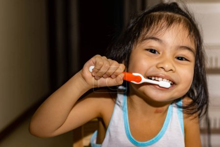 Foto de Pequeña niña asiática mientras se cepilla los dientes. Niño mientras disfruta cepillándose los dientes - Imagen libre de derechos