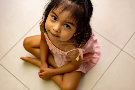 Téléchargez les photos : Mignon petit asiatique fille assis sur un étage et la recherche jusqu ' - en image libre de droit