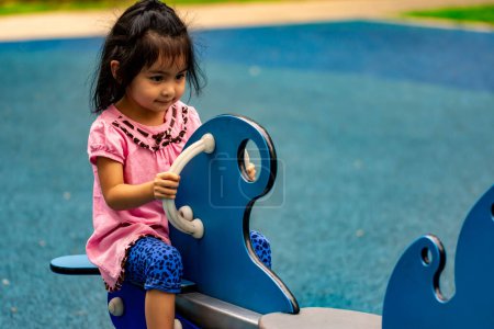 Photo for Pretty asian little girl while sitting and playing on a see saw in a playground - Royalty Free Image