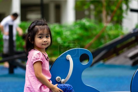 Photo for Pretty asian little girl while sitting and playing on a see saw in a playground - Royalty Free Image