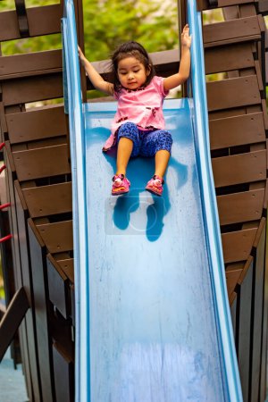 Photo for Pretty asian little girl while sliding in a playground - Royalty Free Image
