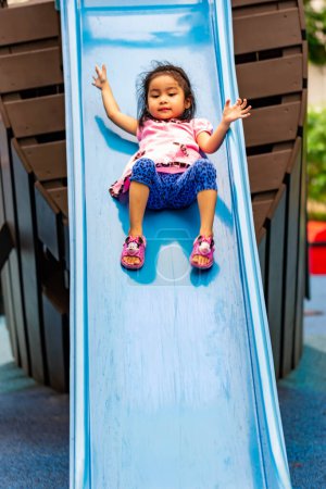 Photo for Pretty asian little girl while sliding in a playground - Royalty Free Image