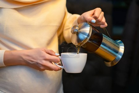Foto de Manos de una chica embarazada sosteniendo una taza en la que se vierte el té - Imagen libre de derechos