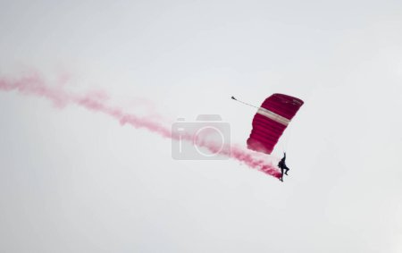 Photo for Silhouette parachute stunt unfocused and blurry while gliding in the air with red smoke trail during an air exhibition - Royalty Free Image