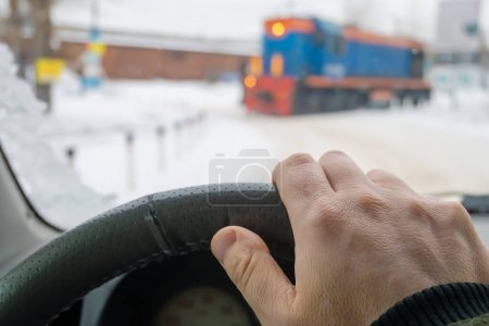 Photo for The driver's hand on the steering wheel of a car that is waiting for a passing train locomotive - Royalty Free Image