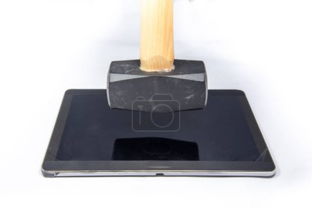 Téléchargez les photos : Un marteau est suspendu verticalement au-dessus d'une tablette numérique - en image libre de droit