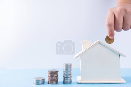 Photo for Hand putting money coin into wooden house with stack coins isolated grey background. Property investment and house mortgage financial concept. - Royalty Free Image