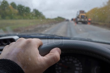 Foto de La mano del conductor en el volante de un coche que pasa por la carretera que se está reparando - Imagen libre de derechos