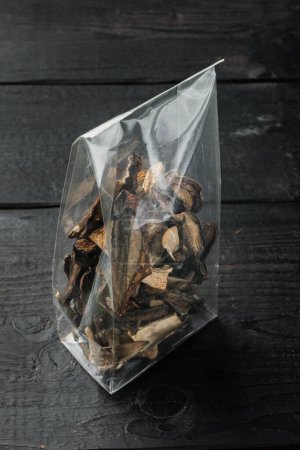 Téléchargez les photos : Mélange de champignons sauvages séchés hachés, sur fond de table en bois noir, en sachet plastique - en image libre de droit