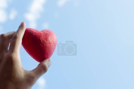 Photo for "Close up Hand holding the red decorative heart against the blue sky." - Royalty Free Image