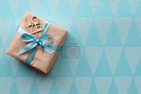 Foto de "Caja de regalo envuelta en papel marrón con cinta azul claro sobre fondo azul. Espacio libre
" - Imagen libre de derechos