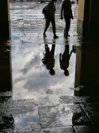 Photo for "People silhouettes reflected in puddle of water after the storm" - Royalty Free Image