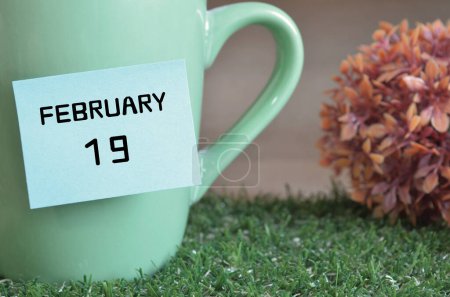 Photo for "close-up shot of cup, sticky note with inscription February 19." - Royalty Free Image