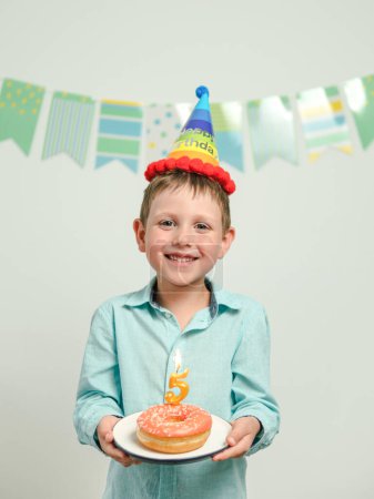 Téléchargez les photos : Donut d'anniversaire avec bougie dans les mains de garçon - en image libre de droit