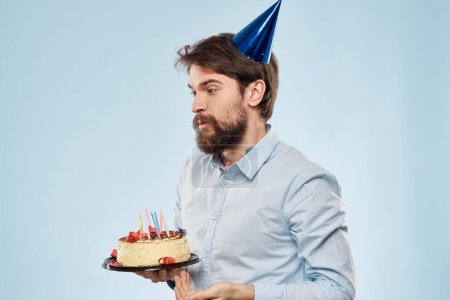 Téléchargez les photos : Un homme en chemise avec un gâteau dans les mains et une casquette festive sur la tête - en image libre de droit