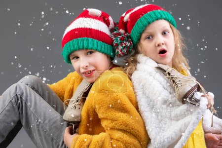 Téléchargez les photos : Petite fille drôle et garçon en bonnets de Noël tricotés et patins à glace vintage - en image libre de droit