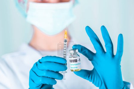Photo for "Doctor or nurse in uniform and gloves wearing face mask protective in lab holding medicine vial vaccine bottle with COVID-19 Coronovirus vaccine label" - Royalty Free Image