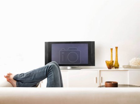 Téléchargez les photos : Jeune homme assis sur le canapé avec la télévision à la maison - en image libre de droit