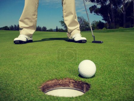 Photo for Male golfer on green with ball at hole in foreground - Royalty Free Image