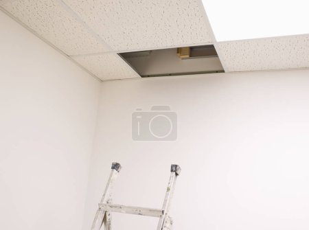 Téléchargez les photos : Échelle en dessous du panneau de plafond ouvert dans le bureau vide - en image libre de droit