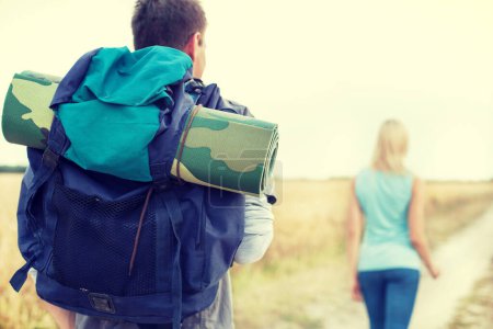 Photo for Young couple with backpacks walking along country road - Royalty Free Image