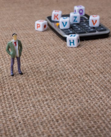 Photo for Letter cubes and a calculator beside a figurine - Royalty Free Image