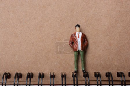 Photo for "The figurine of a little man standing beside spiral notebook" - Royalty Free Image