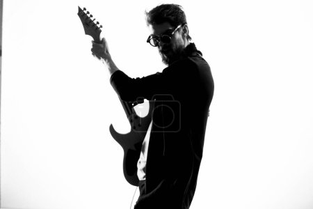 Foto de Alegre músico masculino en chaqueta de cuero con gafas de sol realizando guitarra - Imagen libre de derechos