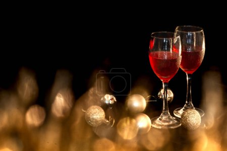 Foto de "Tema de la celebración con dos copas de vino tinto y una bola redonda dorada sobre un pequeño fondo negro dorado" - Imagen libre de derechos
