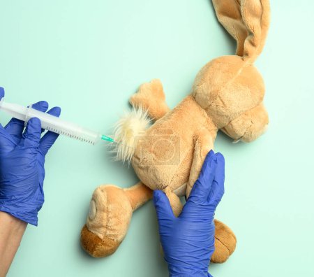 Photo for "plush rabbit and two female hands of a doctor injecting an injection on a blue background" - Royalty Free Image