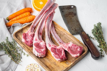 Photo for "Organic pieces of mutton meat, Rack of lamb , raw with bone, with ingredients carrot orange, herbs, and old butcher cleaver knife, on white stone background" - Royalty Free Image