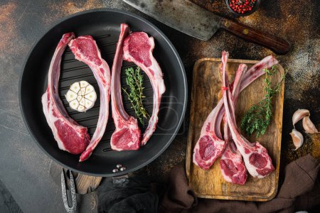Photo for "Frenched raw fatty lamb chops, with ingredients carrot orange, herbs, on frying cast iron pan, on old dark rustic background, top view flat lay" - Royalty Free Image