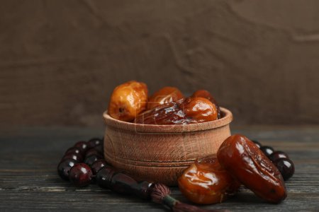 Photo for "Wooden bowl with dates and prayer beads on table against color background" - Royalty Free Image