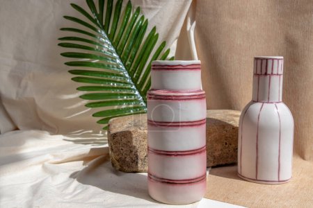 Téléchargez les photos : "Deux vases en céramique blanche et rose faits à la main sur nappe texturée blanche. " - en image libre de droit