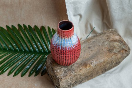 Téléchargez les photos : "Vase en céramique rouge fait à la main sur nappe texturée blanche. " - en image libre de droit