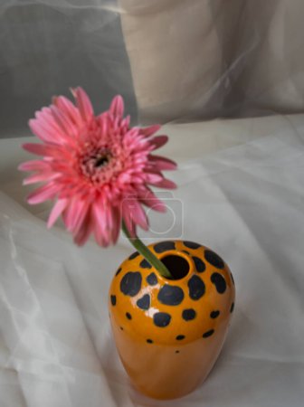 Foto de "Flor rosa en jarrón de cerámica hecho a mano naranja sobre mantel texturizado Blush. " - Imagen libre de derechos