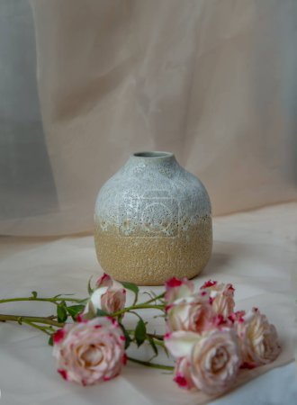 Foto de "Jarrón de cerámica hecho a mano blanco y amarillo con ramo de flores en manteles con textura rubor. " - Imagen libre de derechos