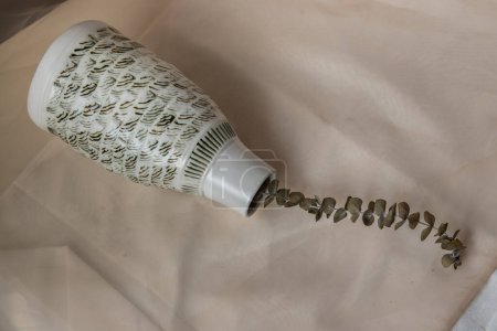 Foto de "Flores secas en forma de botella de jarrón de cerámica blanca en paño de tabla con textura rubor. " - Imagen libre de derechos