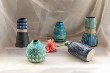 Téléchargez les photos : "Cinq vase en céramique bleu fait à la main avec fleur rose sur nappe texturée Blush. " - en image libre de droit